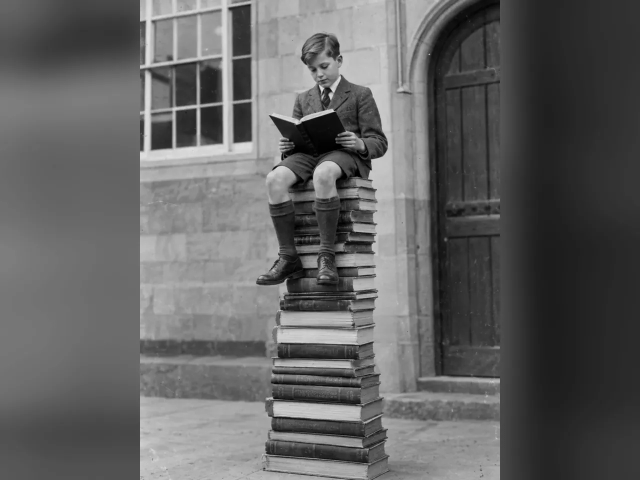 Мальчик читает, сидя на башне из книг
